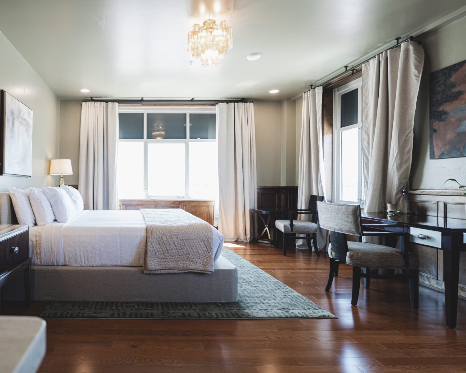 the-ford-suite-bedroom-with-large-windows-drapes-crystal-lighting-desk-area-and-artwork-powerhouse-on-broadway